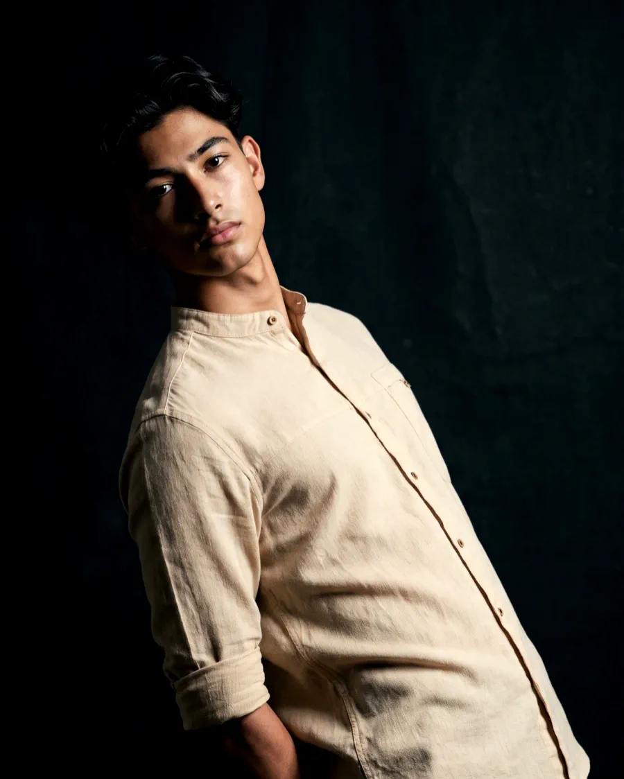 The same cream linen shirt on the same AI model in a dark editorial studio with hard side light