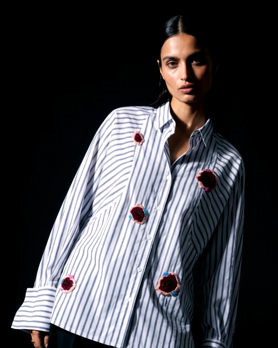 AI generated editorial photo of a woman in an oversized striped shirt with embroidered rose patches against a near black backdrop