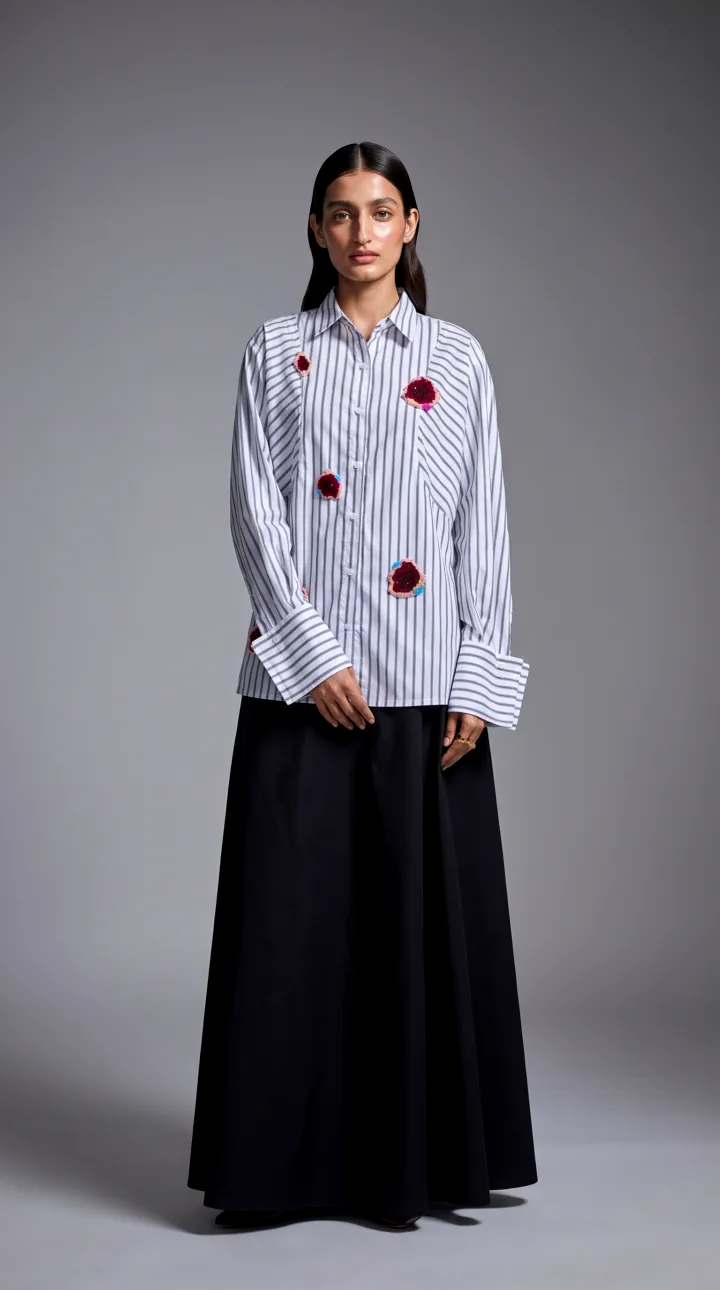 White striped shirt with embroidered rose patches and deep turned-back cuffs, worn by an AI model over a black maxi skirt in a grey studio